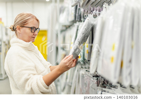 Middle aged woman selecting wallpaper design in home decor section of hardware store Middle aged woman selecting wallpaper design in home decor section of hardware store 140103016