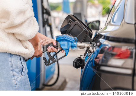 Woman refueling black automobile at gas station with blue fuel pump nozzle during modern transportation and travel activity 140103019