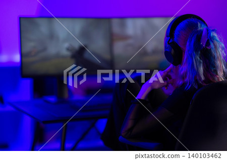Young female gamer focusing on action game in neon-lit gaming setup 140103462