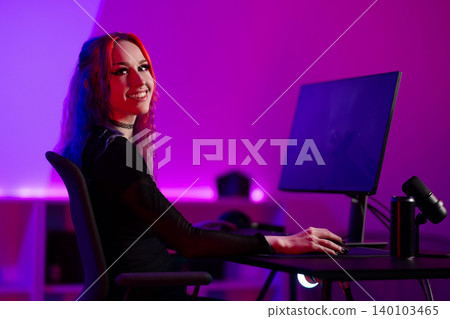 Young female streamer gaming in neon-lit room with microphone and monitor 140103465