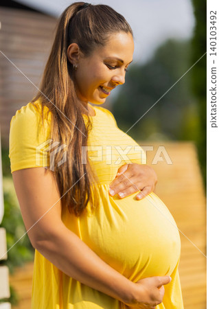 Happy pregnant woman in a bright yellow dress smiling outdoors 140103492
