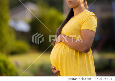 Pregnant Woman in Yellow Dress Posing Outdoors with Calm Expression Pregnant Woman in Yellow Dress Posing Outdoors with Calm Expression 140103495