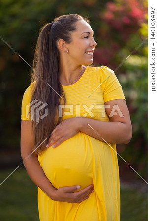 Happy pregnant woman enjoying a sunny day in a yellow dress outdoors Happy pregnant woman enjoying a sunny day in a yellow dress outdoors 140103497