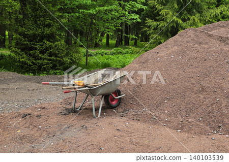 Metal wheelbarrow rests beside a pile of crushed red mulch Metal wheelbarrow rests beside a pile of crushed red mulch 140103539