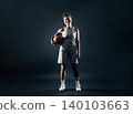 Full length of a young smiling woman professional basketball player holding a ball over a black background 140103663