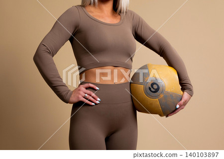 Fit woman in brown workout clothes holding a yellow medicine ball Fit woman in brown workout clothes holding a yellow medicine ball 140103897