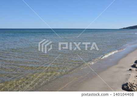 Serene beach landscape featuring soft sand and calm ocean waves under a clear blue sky. The horizon blends seamlessly with the water, creating a peaceful coastal atmosphere Serene beach landscape featuring soft sand and calm ocean waves under a clear blue sky. The horizon blends seamlessly with the water, creating a peaceful coastal atmosphere 140104408