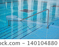 A swimming pool features a stainless steel handrail leading to tiled steps submerged in clear water, with reflections of the surrounding area visible on the water's surface 140104880