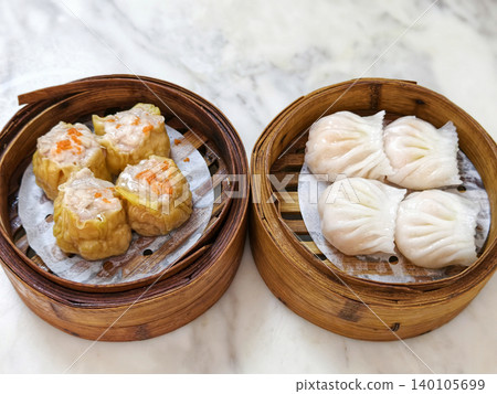 Steamed dim sum assortment featuring siu mai and shrimp dumplings served in traditional bamboo baskets. Steamed dim sum assortment featuring siu mai and shrimp dumplings served in traditional bamboo baskets. 140105699