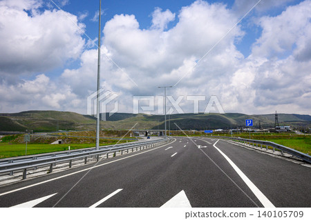 Long straight road with white arrows and guardrails 140105709