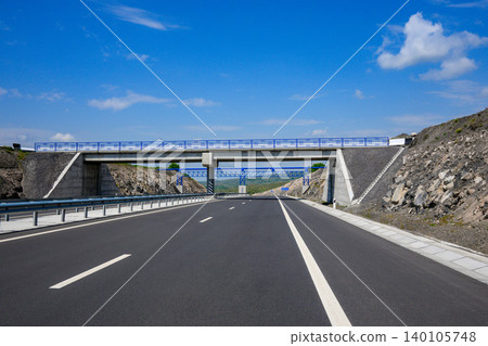 Modern highway stretches forward under bright blue sky Modern highway stretches forward under bright blue sky 140105748
