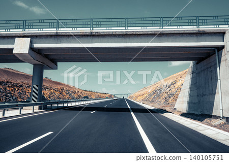 Straight asphalt road passes under large concrete overpass Straight asphalt road passes under large concrete overpass 140105751