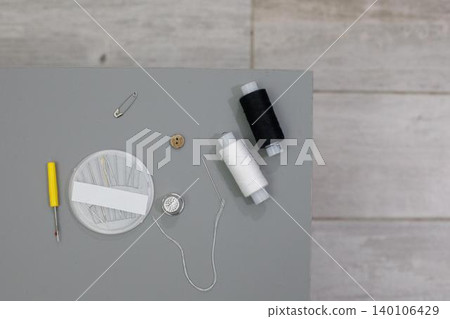Sewing supplies are arranged on a table with thread, needles, and a button for a crafting project 140106429