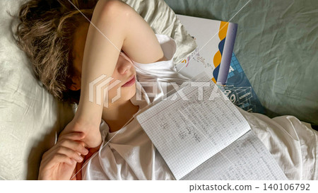 Tired Teenager Lying In Bed With School Notebook And Hand Over Face Tired Teenager Lying In Bed With School Notebook And Hand Over Face 140106792