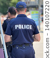 Police officer stands with back to camera during public patrol in urban street. Concept of police presence, law enforcement, security, crowd control, public safety, community protection 140107220