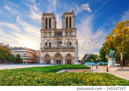 Stunning sunset view of Notre-Dame de Paris with lush greenery and dramatic sky 140107267