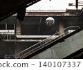 Concrete decay meets modern art in a silent, abandoned space. Neglect is disrupted by a sudden glimmer of life. Weathered concrete and rusted girders frame the hollow interior. A broken escalator cuts 140107337