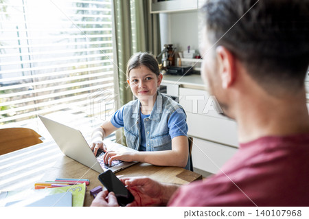Father helping daughter with homework in kitchen. Father helping daughter with homework in kitchen. 140107968