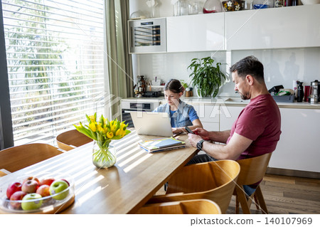 Father helping daughter with homework in kitchen. 140107969