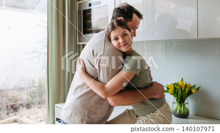 Dad hugging with daughter with diabetes in kitchen at home. 140107971