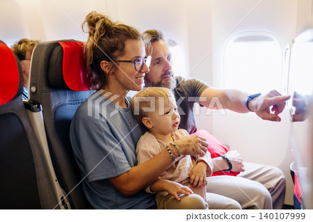 Parents calming upset child during family flight, watching cartoons. Plane traveling. Parents calming upset child during family flight, watching cartoons. Plane traveling. 140107999