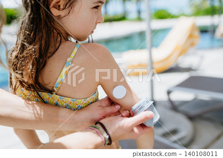 Mother changing glucose sensor for diabetic daughter by pool. 140108011