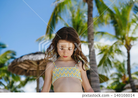 Smiling little girl standing under palm tree during sunny summer vacation. Smiling little girl standing under palm tree during sunny summer vacation. 140108014