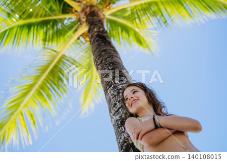 Smiling little girl standing under palm tree during sunny summer vacation. Smiling little girl standing under palm tree during sunny summer vacation. 140108015