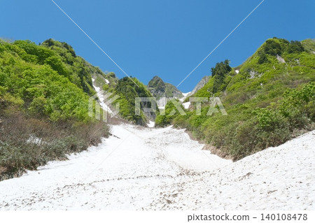初夏時節的山景，鬱鬱蔥蔥的綠色山坡，湛藍的天空延伸到白雪皚皚的山丘之外。 140108478