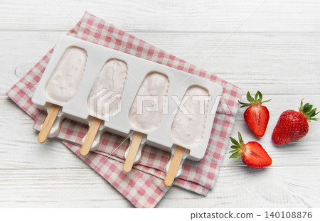Diy strawberry yogurt popsicles chilling in mold on white wood Diy strawberry yogurt popsicles chilling in mold on white wood 140108876
