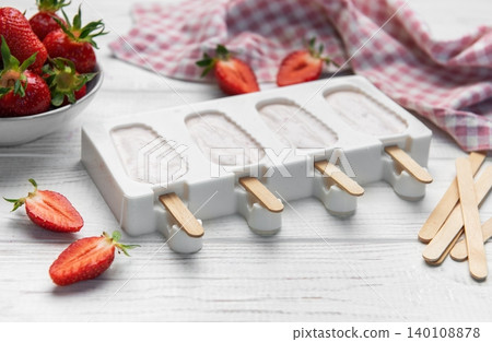 Strawberry popsicles in making process on white wooden surface Strawberry popsicles in making process on white wooden surface 140108878
