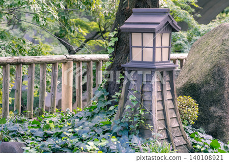 A horizontal composition of a stone lantern in front of a large tree. A horizontal composition of a stone lantern in front of a large tree. 140108921