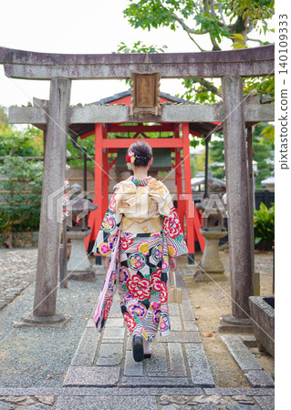 The back view of a woman in a floral kimono walking towards the torii gate of a shrine. Kyoto, Koinari Daimyojin Shrine. The back view of a woman in a floral kimono walking towards the torii gate of a shrine. Kyoto, Koinari Daimyojin Shrine. 140109333