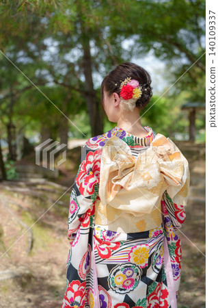 The back view of a woman in a brightly colored kimono, gazing out at a garden lush with new greenery. Kyoto, Japan The back view of a woman in a brightly colored kimono, gazing out at a garden lush with new greenery. Kyoto, Japan 140109337