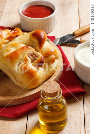 A traditional baked savory closed esfiha with olives, lemon, ketchup, and olive oil, served on a round wooden plate with a red napkin A traditional baked savory closed esfiha with olives, lemon, ketchup, and olive oil, served on a round wooden plate with a red napkin 140109356
