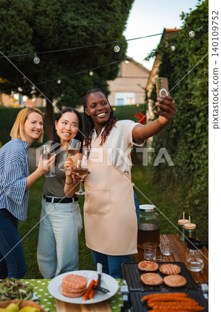 Diverse adult friends taking selfie enjoying outdoor BBQ garden party Diverse adult friends taking selfie enjoying outdoor BBQ garden party 140109752