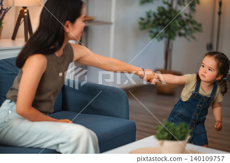 Mother holding daughter's hand pulling away at home Mother holding daughter's hand pulling away at home 140109757