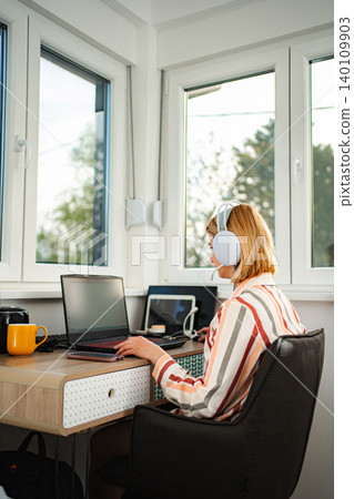 Woman working from home connecting with laptop and headphones Woman working from home connecting with laptop and headphones 140109903