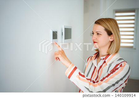 Woman adjusting smart thermostat controlling home climate 140109914