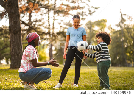 Family playing soccer outdoors in a park enjoying moment Family playing soccer outdoors in a park enjoying moment 140109926