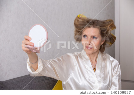 Woman in silk robe checking her hairstyle in a mirror at home during daytime Woman in silk robe checking her hairstyle in a mirror at home during daytime 140109937