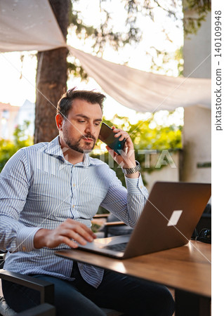 Man working remotely outdoors using laptop and smartphone 140109948