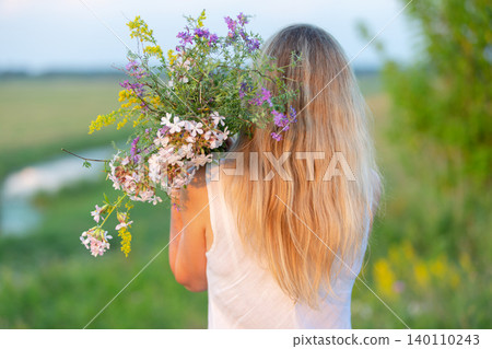 Woman carrying a large bouquet of wildflowers in a lush green field during sunset Woman carrying a large bouquet of wildflowers in a lush green field during sunset 140110243