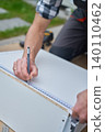Man marks measurements on drawer panel with ruler and pen outdoors 140110462