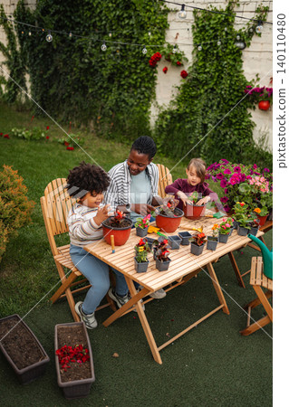 Mother and children potting flowers together in backyard Mother and children potting flowers together in backyard 140110480
