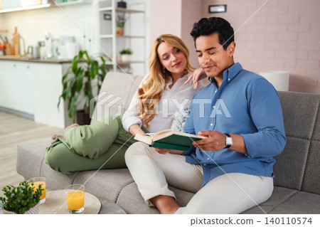 Couple enjoying leisure time reading book on couch Couple enjoying leisure time reading book on couch 140110574