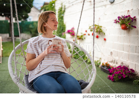 Woman relaxing in swing chair with coffee cup in garden 140110578