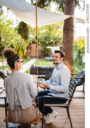 Couple sitting outdoors talking and smiling in garden Couple sitting outdoors talking and smiling in garden 140110599