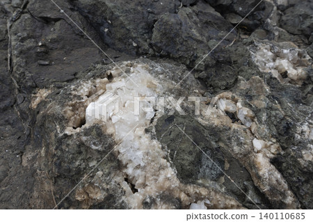 Close-up of a raw calcite mineral formation embedded within a dark rock matrix Close-up of a raw calcite mineral formation embedded within a dark rock matrix 140110685