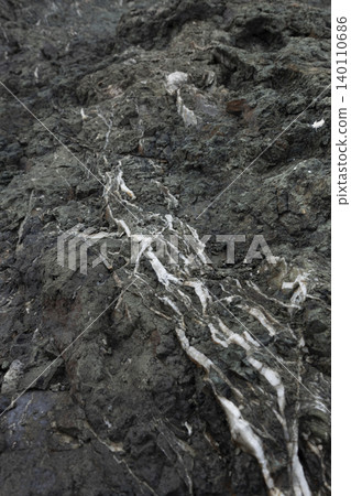 Close-up of white quartz veins branching through a dark, rugged rock surface Close-up of white quartz veins branching through a dark, rugged rock surface 140110686